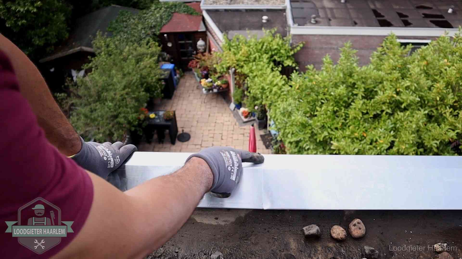 Vakman plaatst een daktrim op de dakrand van een woning in Haarlem