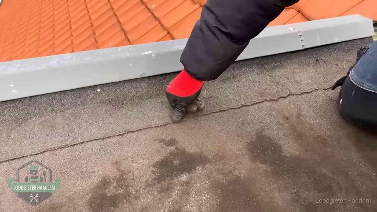 Vakman wijst een naad met vochtplekken aan op een bitumen plat dak in Haarlem