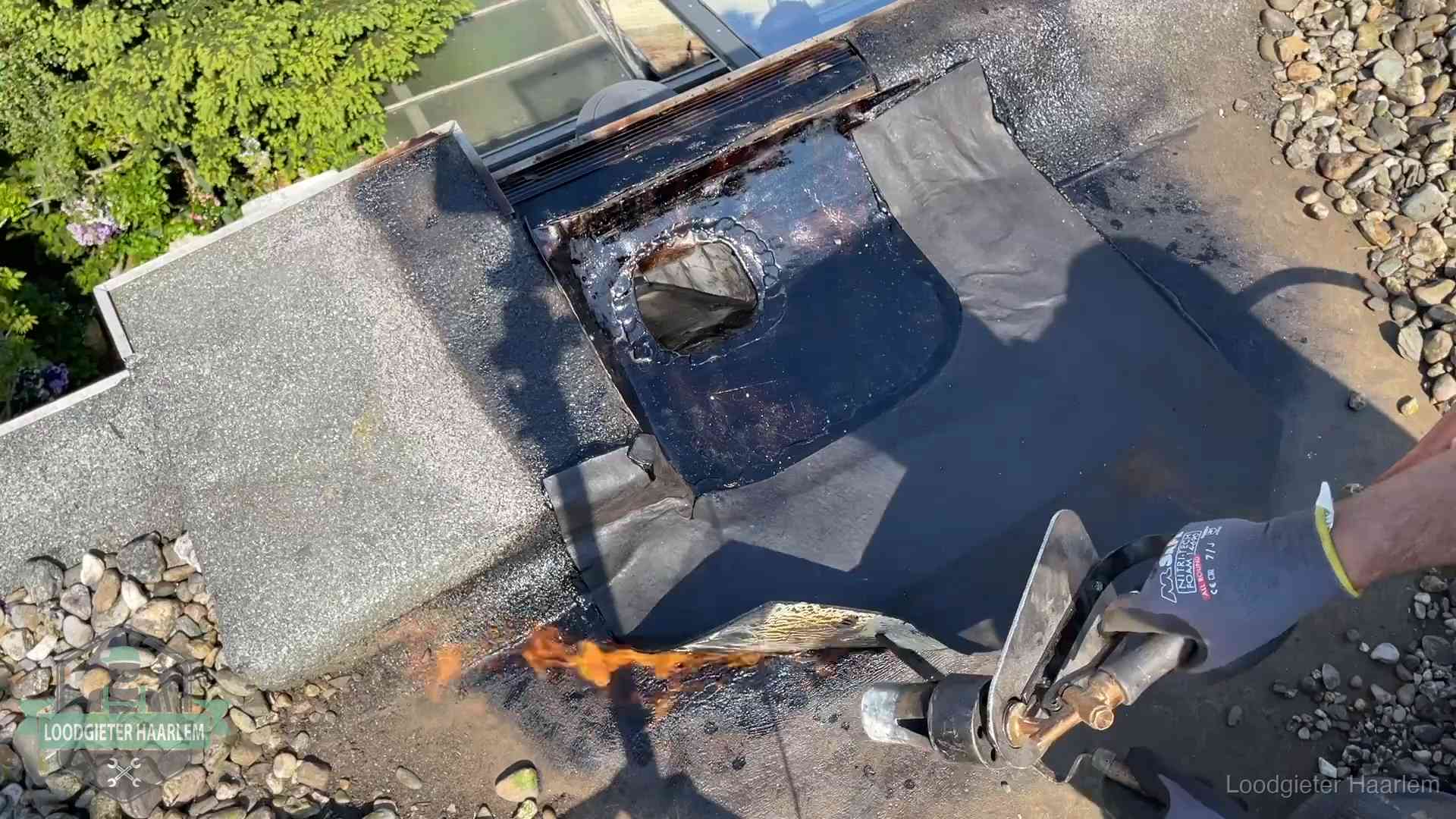 Dakdekker brandt bitumen rond een doorvoer tijdens een daklekkage-reparatie in Haarlem