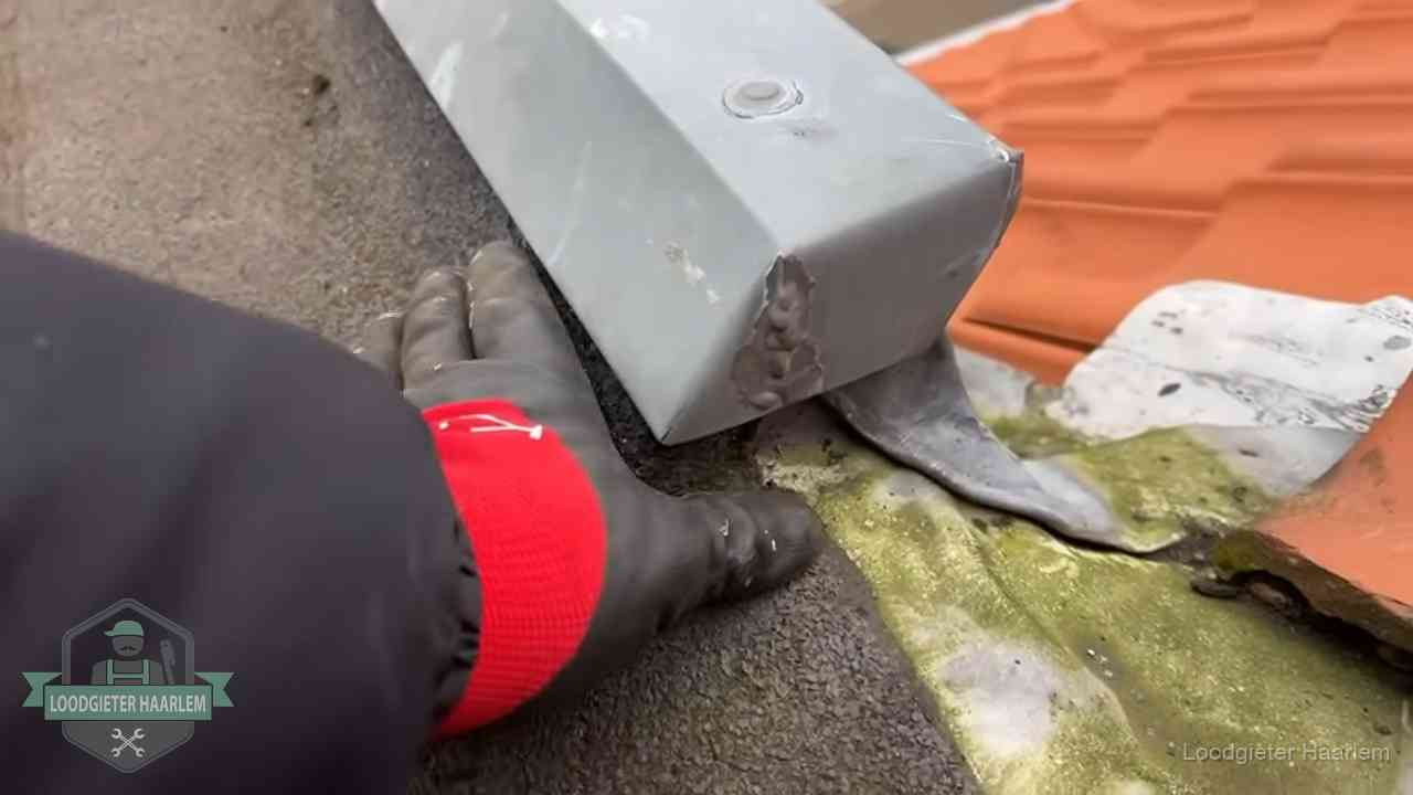 Controle van een zinken hemelwaterafvoer met loodslab bij dakpannen in Haarlem