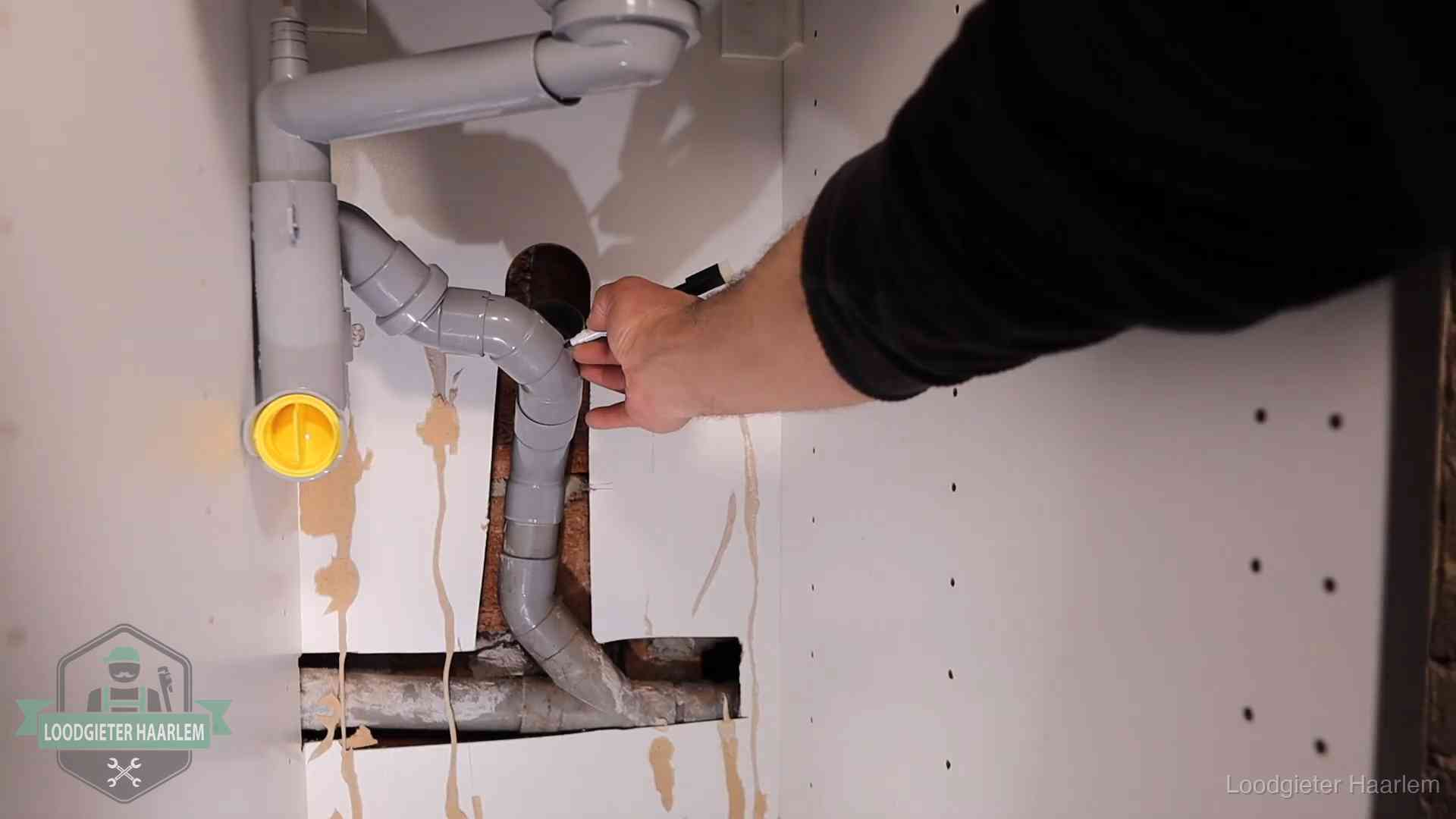 Loodgieter voor verhuurders en bedrijven in Haarlem Loodgieter markeert een pvc-afvoerbuis onder een gootsteen in Haarlem