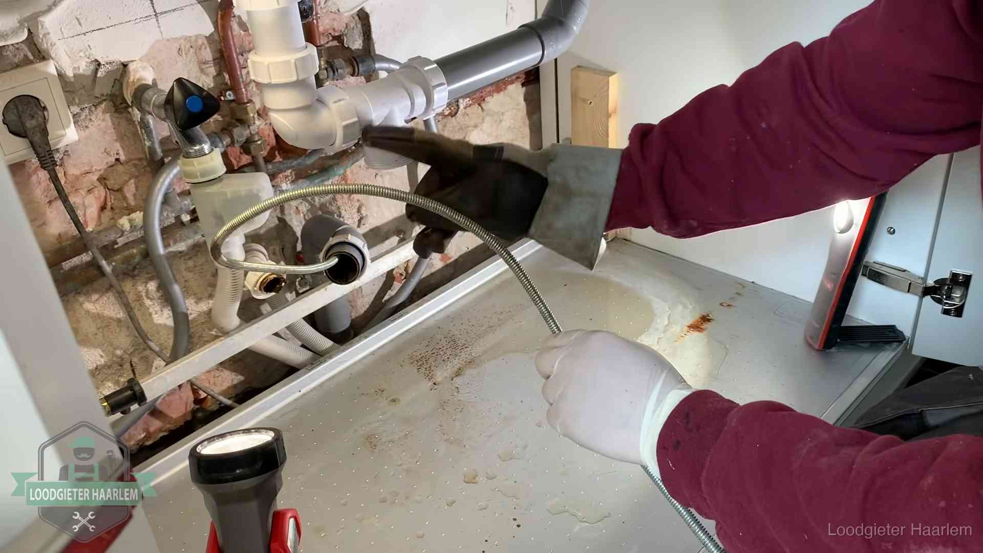 Spiraal of hogedruk in Haarlem Ontstoppingsveer gaat in een geopende sifonaansluiting onder het aanrecht in Haarlem
