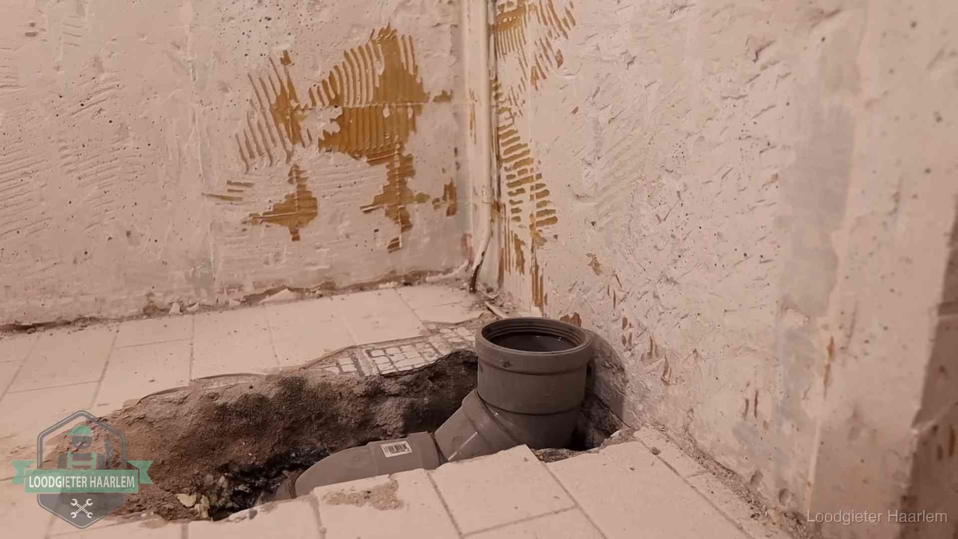 Verzakt riool herstellen in Haarlem Opengebroken vloer met een nieuwe pvc-rioolbocht in een gegraven sleuf in Haarlem