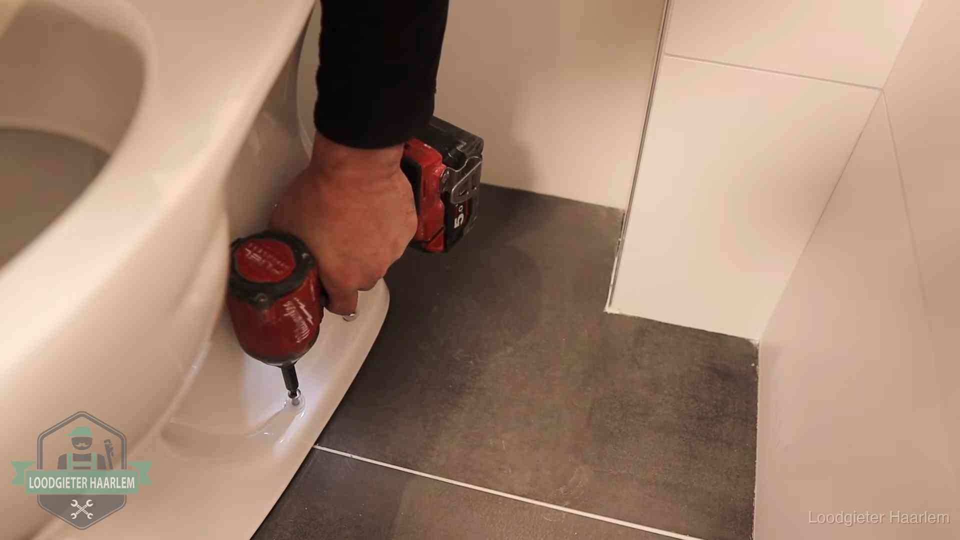 Loodgieter zet de voet van een wc-pot vast op de tegelvloer in Haarlem